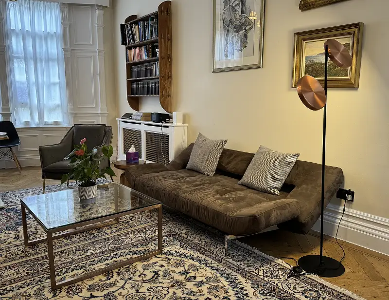Harley Street Therapy London A cosy living room features a brown sofa with two cushions, a glass coffee table with a plant, and wall art—creating a relaxing space reminiscent of the calm you’ll find when you contact London Trusted Therapy on Harley Street.