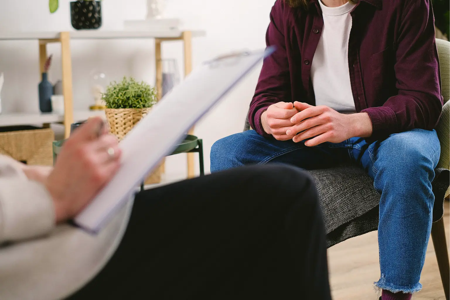 Cultural Humility in Therapy London Trusted Therapy A person sits with hands clasped, facing another person holding a clipboard and taking notes, suggesting a therapy or counselling session that values cultural humility in a comfortable room.
