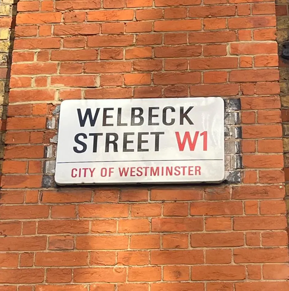 A street sign on a red brick wall reads WELBECK STREET W1 with CITY OF WESTMINSTER written below in red letters.